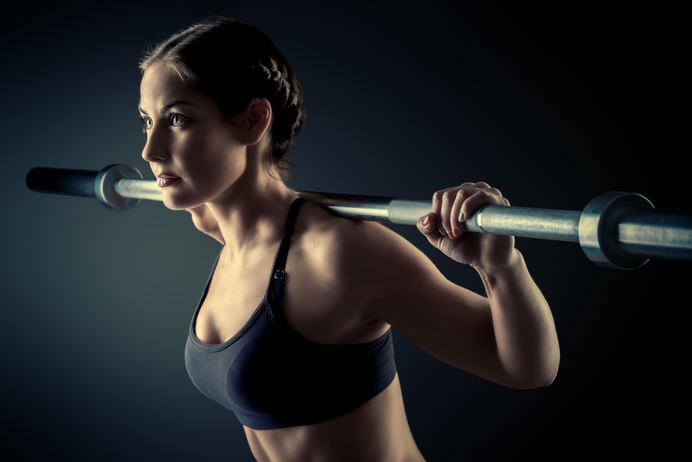 Athletic woman training with a barbell in a dark premium gym setting
